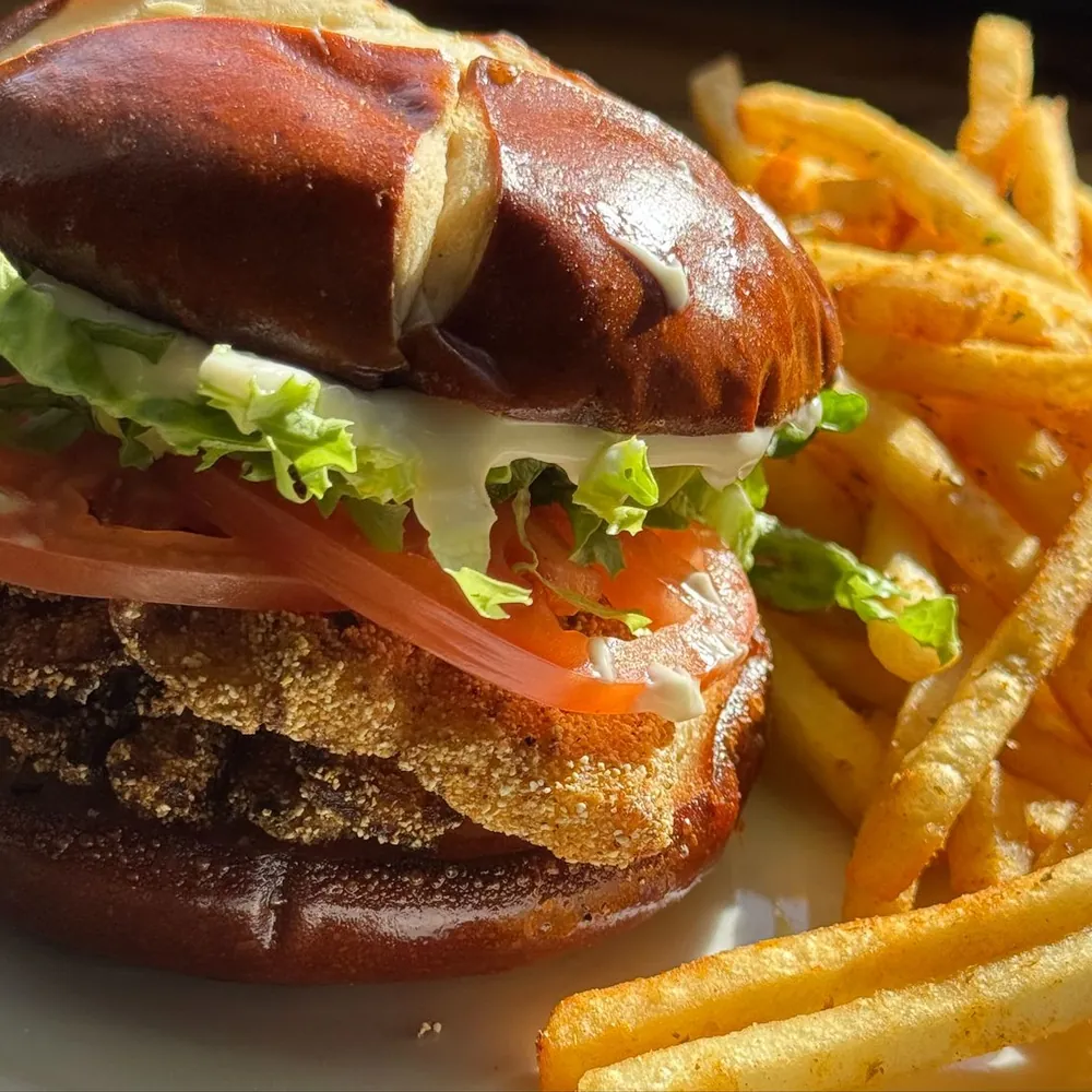 Cornmeal-crusted catfish sandwich on a pretzel bun with lettuce, tomato and mayo, next to seasoned fries