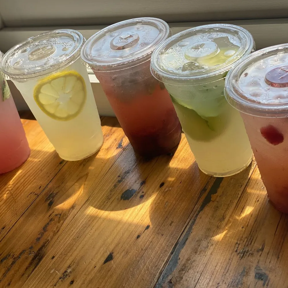 A row of house-made lemonades in five flavors, lined up on a sunlit wooden windowsill