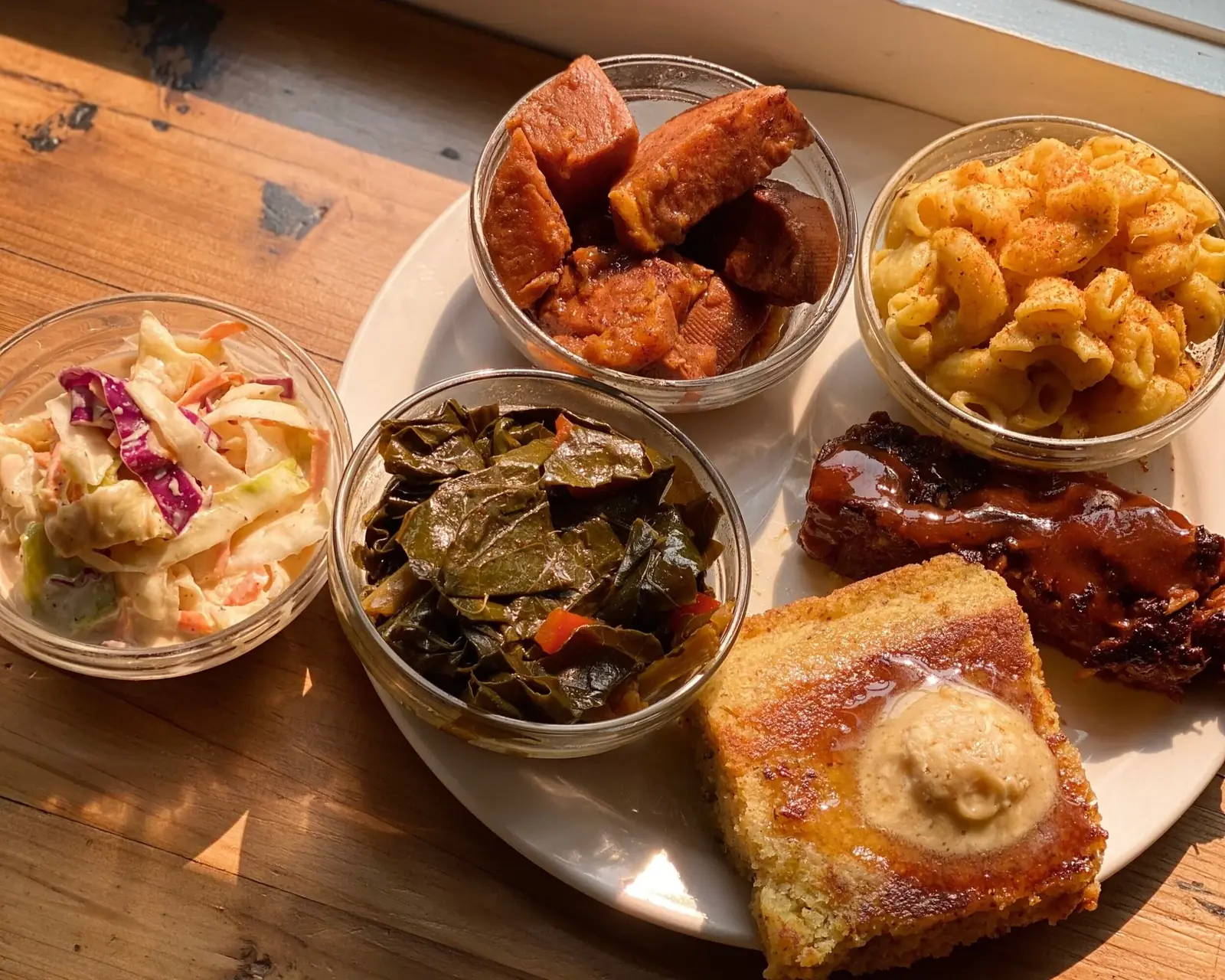 A plant-based soul food platter — mac and cheese, collard greens, candied yams, BBQ jackfruit ribs, slaw and cornbread